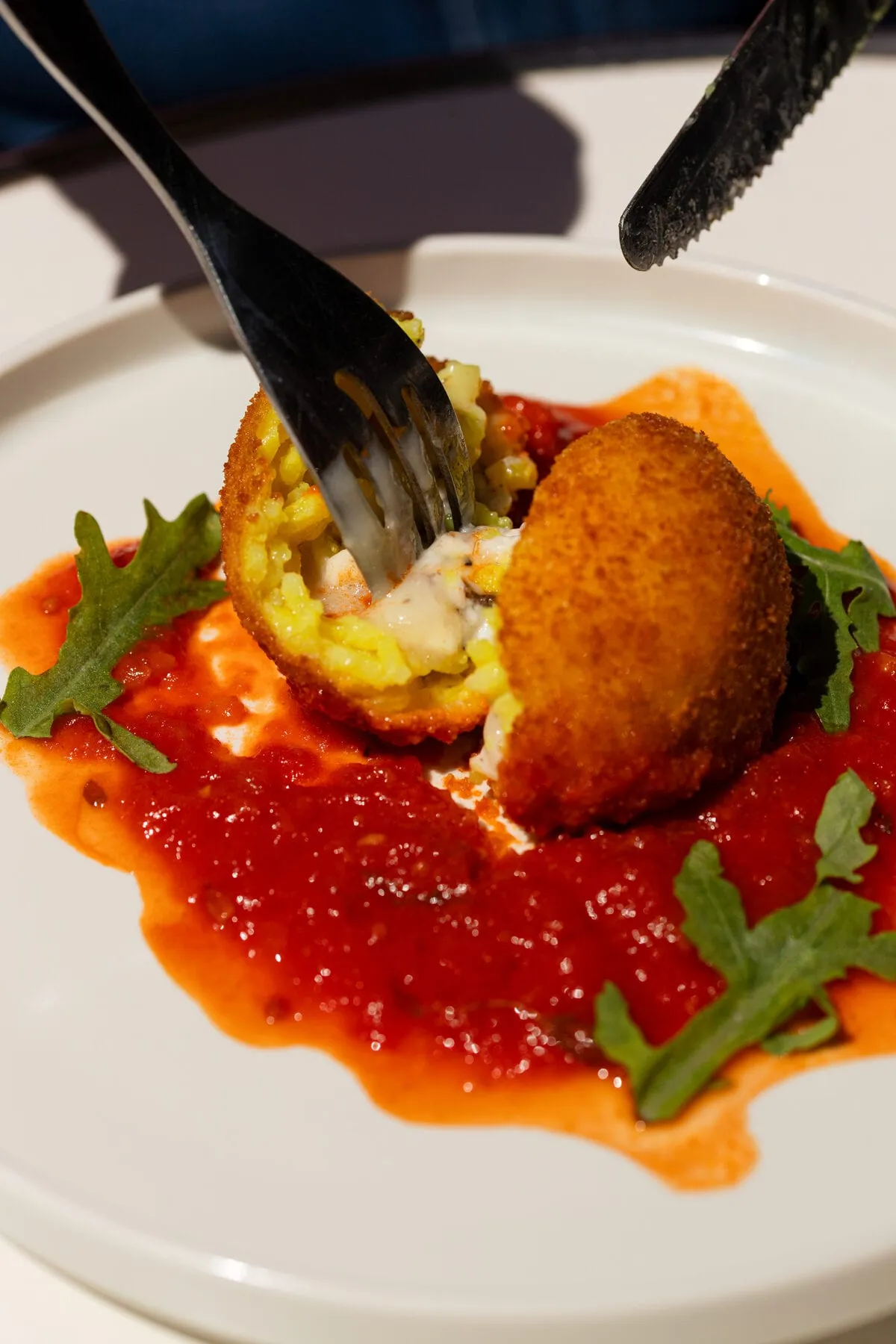 Arancini au riz safrané ouvert à la fourchette, cœur fondant, sur sauce tomate et roquette