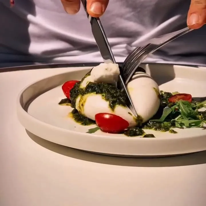 Une burrata au pesto verde qu’on ouvre au couteau, le cœur crémeux qui s’échappe, tomates cerises et roquette