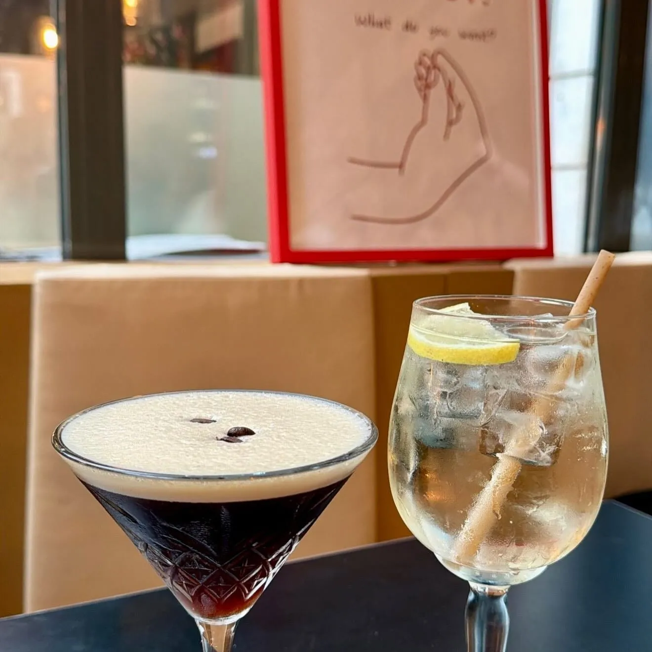 Un espresso martini et un gin tonic au citron sur une table de la salle, devant une affiche dessinée posée sur la banquette