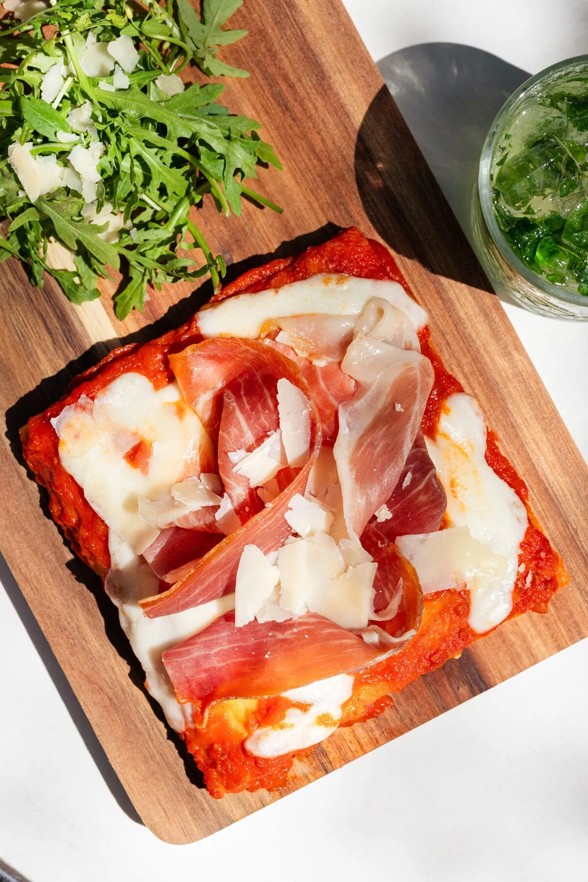 Foccapizza au jambon de Parme, fior di latte et copeaux de parmesan sur une planche en bois, roquette et mojito à côté
