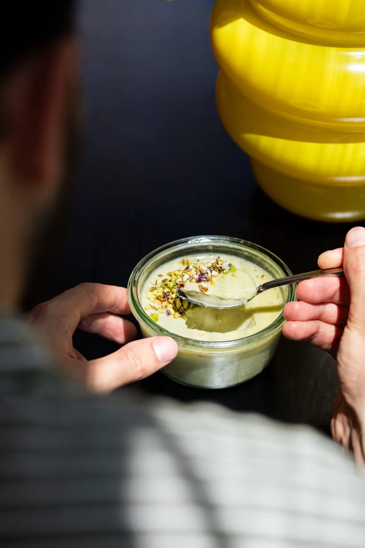 Crème à la pistache en pot de verre, éclats de pistache, tenue à deux mains