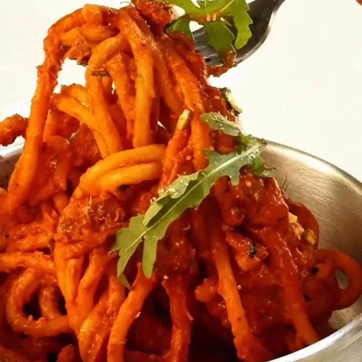 Des spaghetti à la sauce tomate et à la roquette s’enroulent sur une fourchette, au-dessus du poêlon