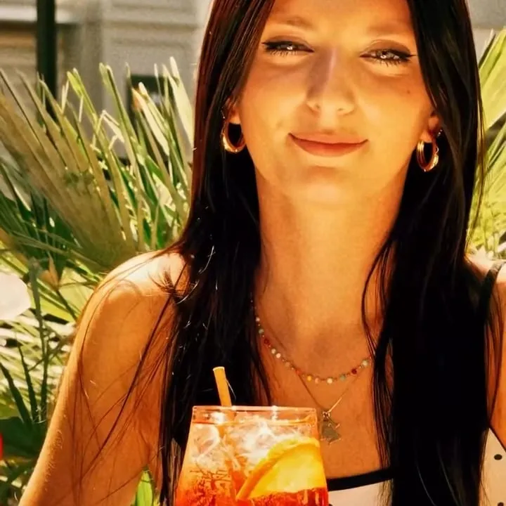 Une cliente sourit en terrasse, un spritz devant elle, entre les palmiers